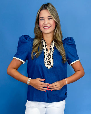 Woman wearing a blue blouse with leopard print details against a blue background