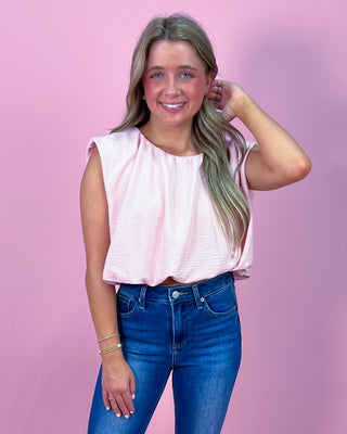 Woman wearing a pink top and blue jeans against a pink background