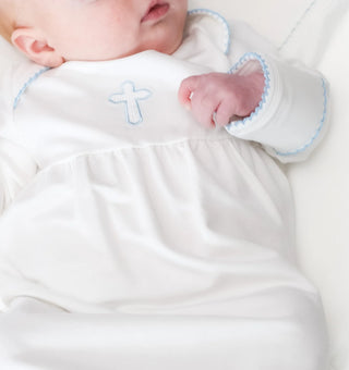 Newborn baby in a white outfit with blue trim and cross design on a white background