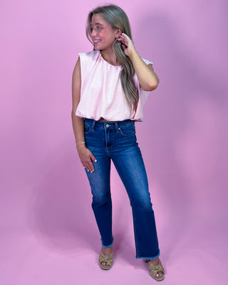 Woman wearing a pink sleeveless top and blue jeans against a pink background
