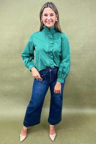 Woman wearing a green blouse and blue jeans against a green background
