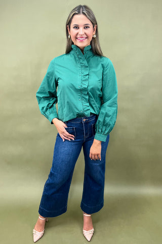 Woman wearing a green blouse and blue jeans against a green background