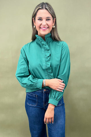 Woman wearing a green blouse with ruffled details and blue jeans against a beige background