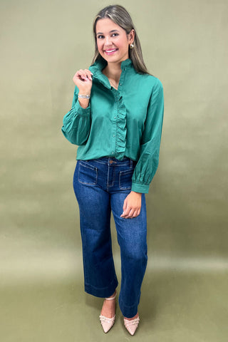Woman wearing a green blouse and blue jeans on a plain background