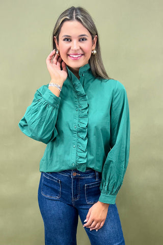 Woman wearing a green blouse with ruffled details and blue jeans against a beige background