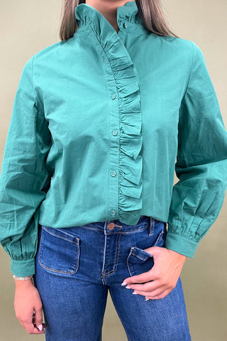 Person wearing a teal blouse with ruffled details and blue jeans against a beige background