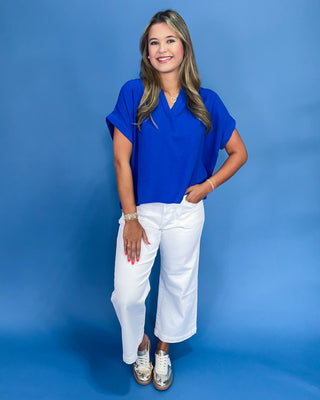 Woman wearing a blue shirt and white pants against a blue background