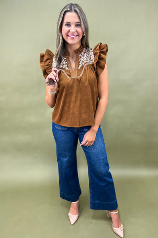 Woman wearing a brown top with ruffled sleeves and blue jeans on a green background