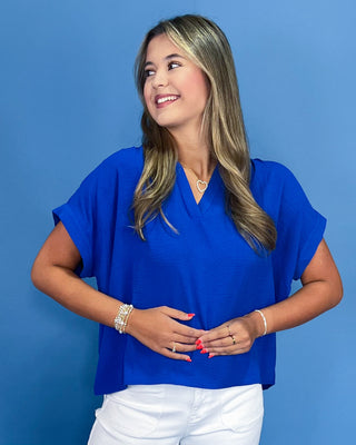 Woman wearing a blue top and white pants against a blue background