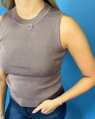 A woman wearing a sleeveless ribbed knit top in a muted taupe-brown color, paired with blue jeans