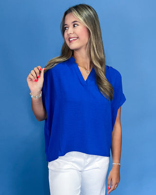 Woman wearing a blue top and white pants against a blue background