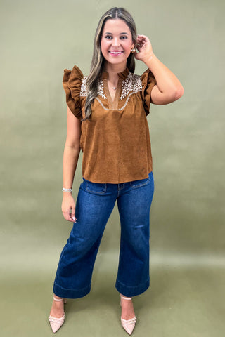 Rust brown corduroy blouse with ruffled sleeves and white floral embroidery paired with dark wash wide-leg jeans for a chic fall look