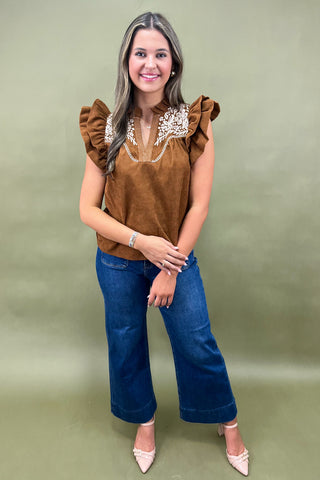 Woman wearing a brown top with ruffled sleeves and blue jeans on a green background