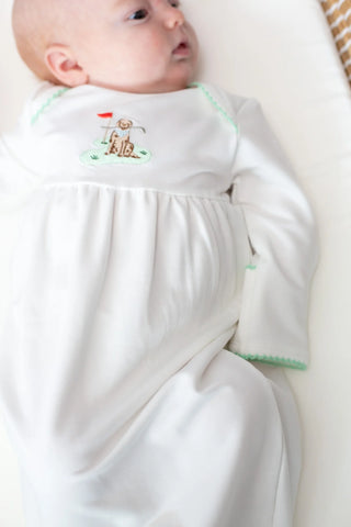Baby wearing a white outfit with green trim and embroidered design on a white background