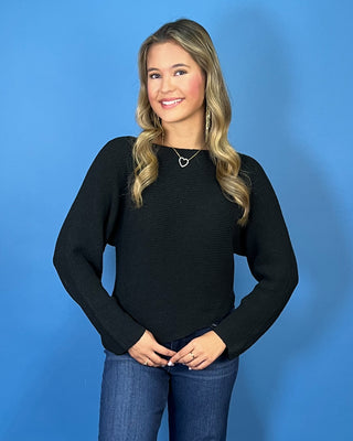 Black long sleeve knit sweater with a classic round neckline, subtle textured finish, relaxed fit, and slightly curved hem.