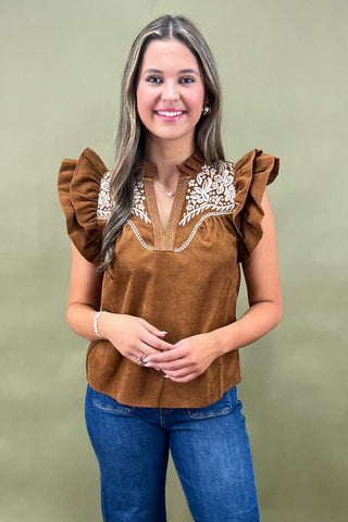 Woman wearing a brown blouse with ruffled sleeves and white embroidery on a green background