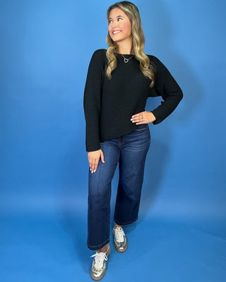 Black long sleeve knit sweater with a classic round neckline, subtle textured finish, relaxed fit, and slightly curved hem.