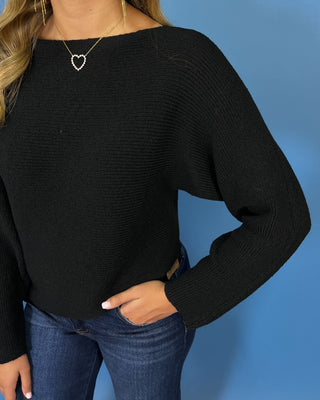 Black long sleeve knit sweater with a classic round neckline, subtle textured finish, relaxed fit, and slightly curved hem.