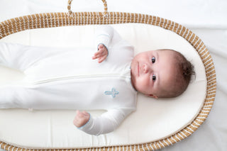Newborn baby in a white outfit lying in a wicker Moses basket.