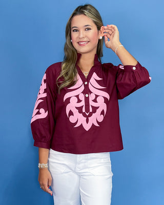 Woman wearing a maroon blouse with pink tribal design against a blue background