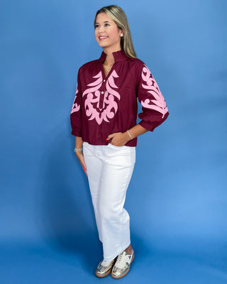 Woman wearing a maroon jacket with pink patterns against a blue background