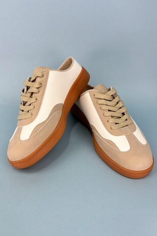Pair of beige and white sneakers with brown soles on a light blue background