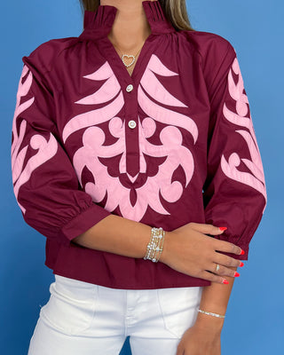 Maroon blouse with pink patterns worn by a person against a blue background