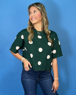 Forest green short sleeve knit sweater with oversized ivory polka dots, a classic crew neckline, ribbed trim, and a relaxed fit.