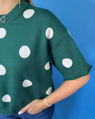 Forest green short sleeve knit sweater with oversized ivory polka dots, a classic crew neckline, ribbed trim, and a relaxed fit.