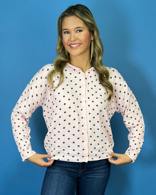Light pink button-front knit cardigan with chocolate brown polka dots, a round neckline, long sleeves, and a relaxed fit.