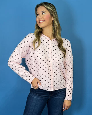 Light pink button-front knit cardigan with chocolate brown polka dots, a round neckline, long sleeves, and a relaxed fit.
