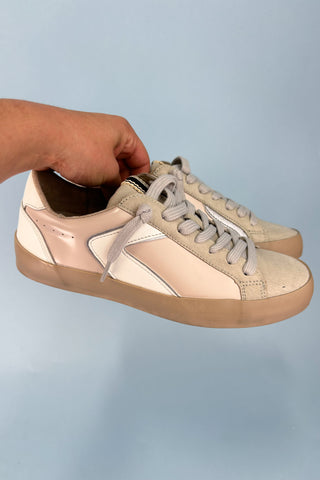 Beige and white sneakers with a hand holding one shoe against a light blue background