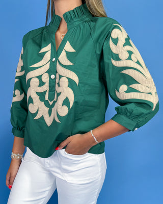 Green blouse with beige embroidery worn by a person on a blue background