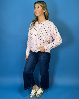 Light pink button-front knit cardigan with chocolate brown polka dots, a round neckline, long sleeves, and a relaxed fit.