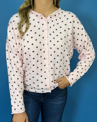 Light pink button-front knit cardigan with chocolate brown polka dots, a round neckline, long sleeves, and a relaxed fit.