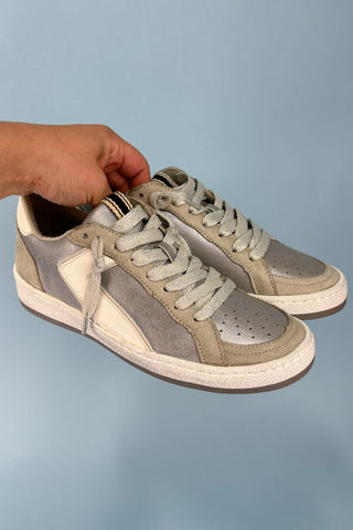 Gray and beige sneakers held by a hand against a light blue background