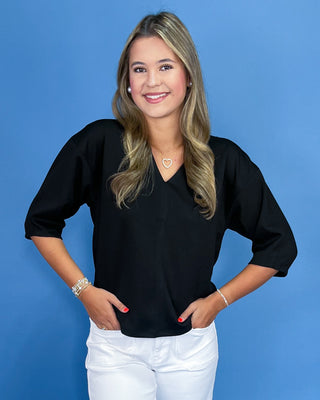 Woman wearing a black top and white pants against a blue background