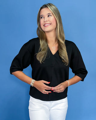 Woman wearing a black top and white pants against a blue background