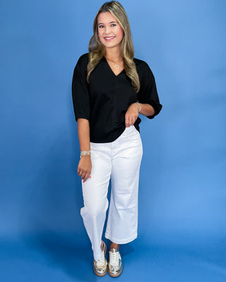 Woman wearing a black top and white pants against a blue background