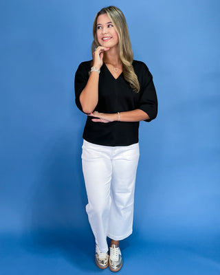 Woman wearing a black top and white pants against a blue background