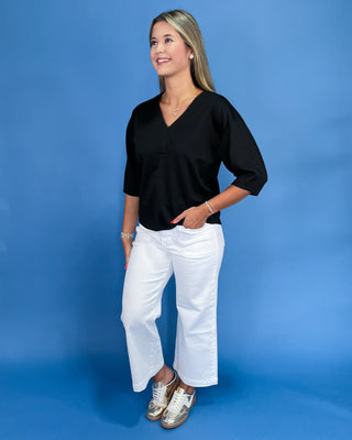 Woman wearing a black top and white pants against a blue background