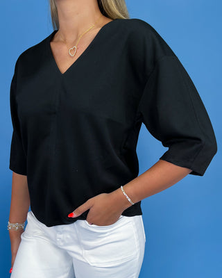 Person wearing a black top and white pants against a blue background