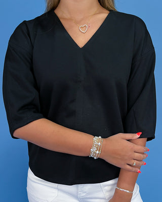 Person wearing a black top with white pants against a blue background