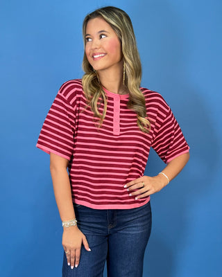 Pink and burgundy striped short sleeve knit top with a round neckline, button placket, relaxed fit, and contrast pink trim.