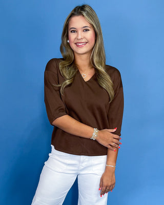 Woman wearing a brown top and white pants against a blue background