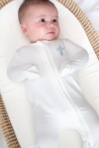 Baby in a white christening gown with a cross emblem, lying on a textured surface.