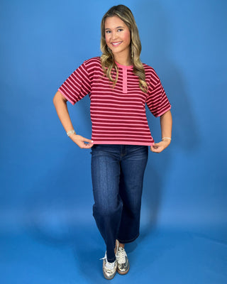 Pink and burgundy striped short sleeve knit top with a round neckline, button placket, relaxed fit, and contrast pink trim.