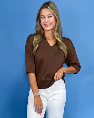 Woman wearing a brown top and white pants against a blue background
