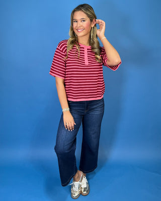 Pink and burgundy striped short sleeve knit top with a round neckline, button placket, relaxed fit, and contrast pink trim.