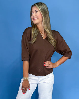 Woman wearing a brown top and white pants against a blue background